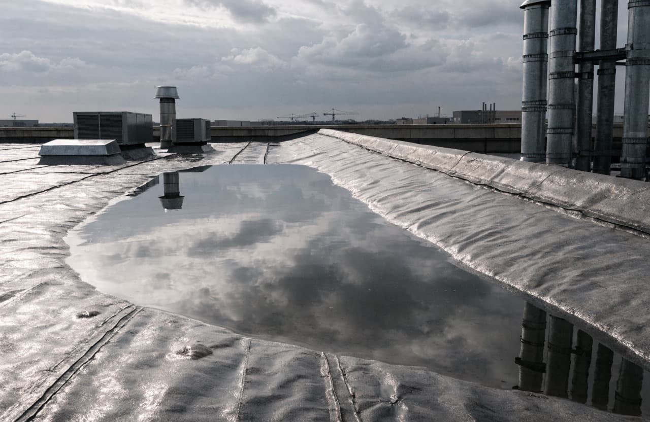 Ponding water and aged seams on a flat commercial roof membrane after a storm
