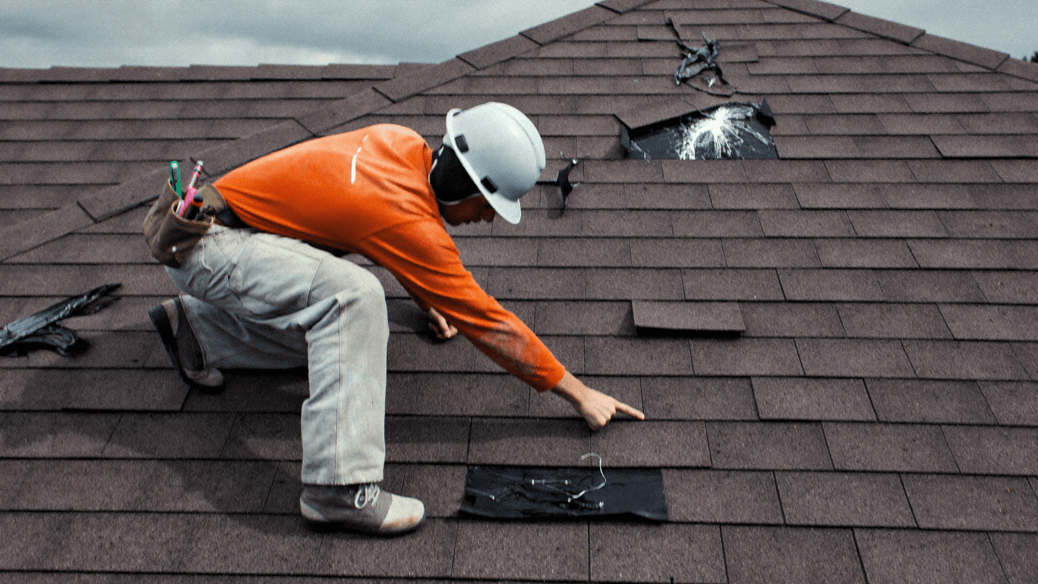 Roofer examining hail-damaged shingles on a residential roof