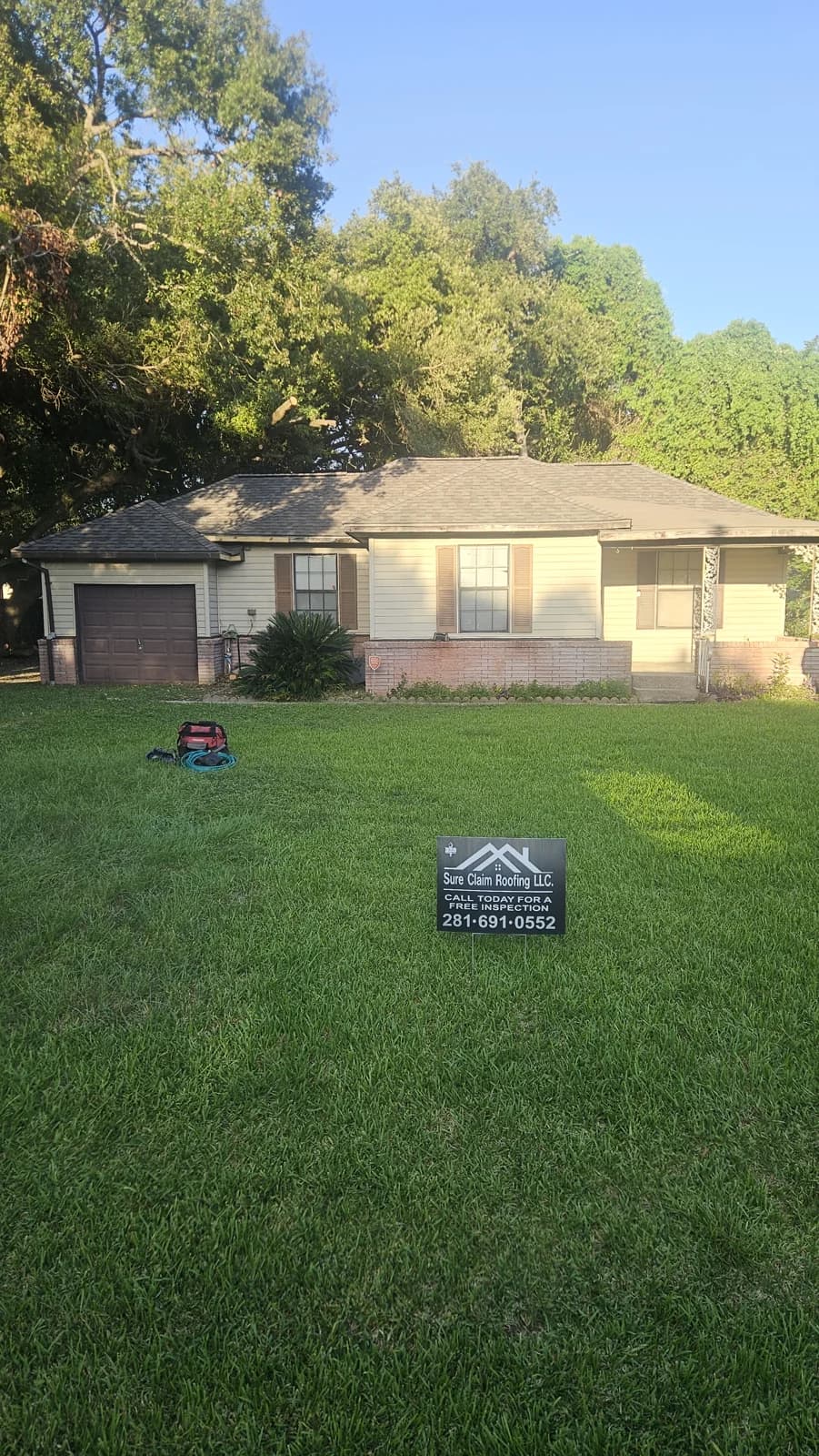 Front view of the Baytown home after roof replacement, with a Sure Claim Roofing sign in the yard